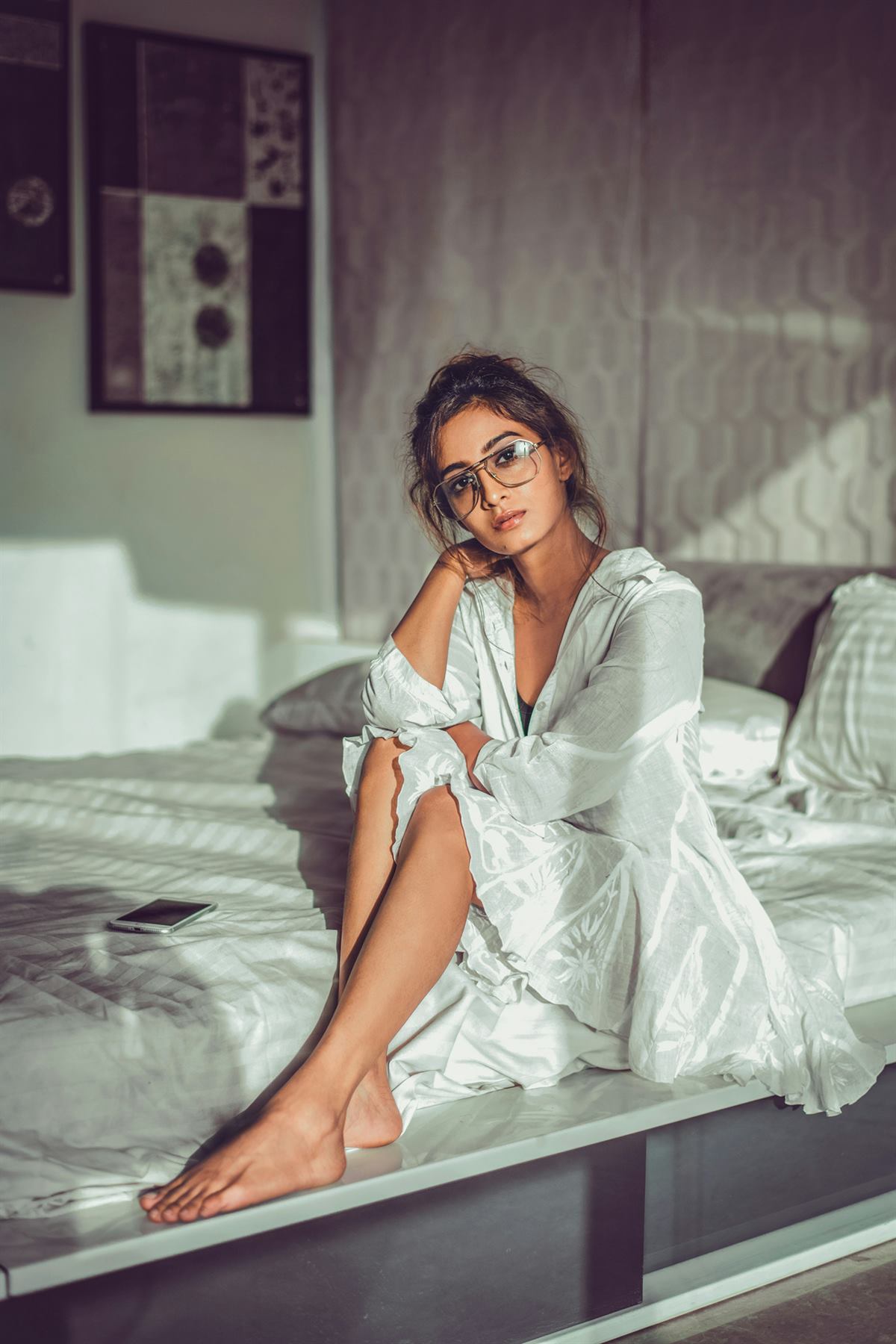 Frau mit Brille sitzt morgens entspannt auf dem Bett